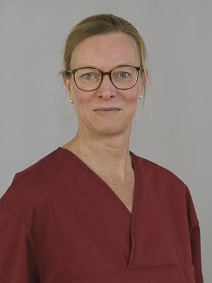 Es ist eine Person in medizinischer Kleidung mit Brille und rotem Oberteil.