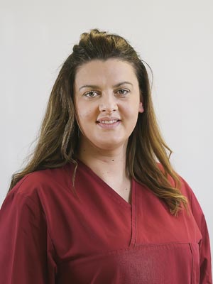 Eine Person trägt ein rotes Oberteil und lächelt in die Kamera vor neutralem Hintergrund.