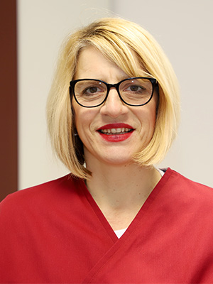 Eine Frau mit blonden Haaren, Brille und rotem Oberteil lächelt in die Kamera.