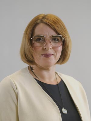 Es zeigt eine Person mit kurzem, braunem Haar und Brille, die neutral in die Kamera schaut.