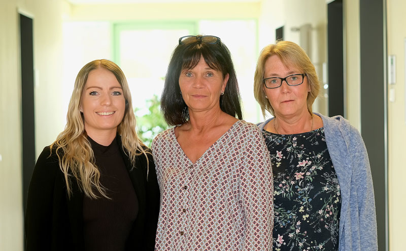 Drei Frauen stehen in einem Flur und lächeln in die Kamera.