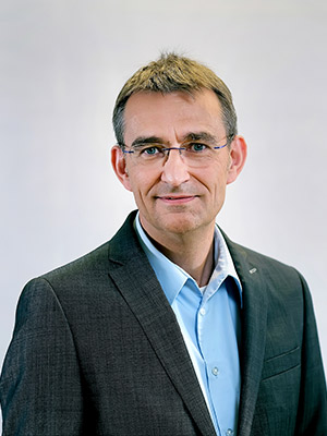 Eine Person in einem Anzug und Hemd, die freundlich in die Kamera schaut.