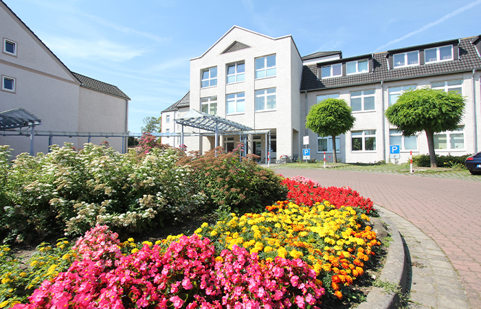 Ein Gebäude mit einem bunten Blumenbeet im Vordergrund und Bäumen auf einem Parkplatz.